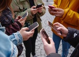 Circle of teenagers holding smartphones - Multicultural young individuals using mobile phones outdoors - Concept of teenagers addicted to new technology