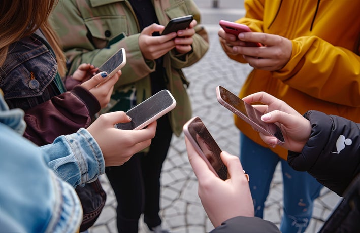 Circle of teenagers holding smartphones - Multicultural young individuals using mobile phones outdoors - Concept of teenagers addicted to new technology