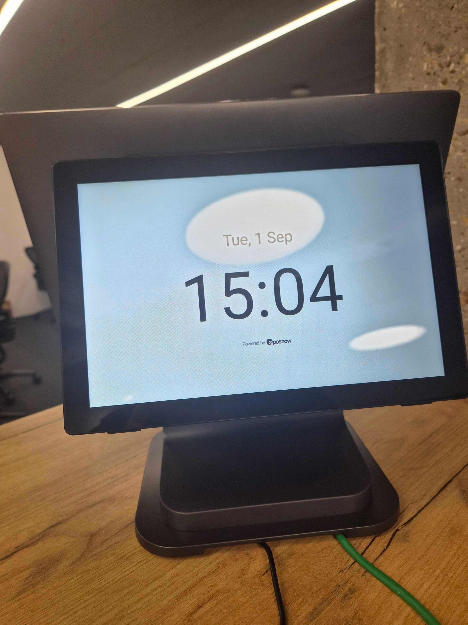 A customer-facing secondary display on the Epos Now Countertop 2 terminal mounted on a wooden counter, showing a clock screen with the time 15:04 and date Tue, 1 Sep.